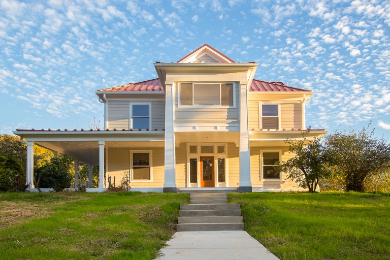 Exterior photo of the front of a 2-story house with yellow siding and a red roof.
