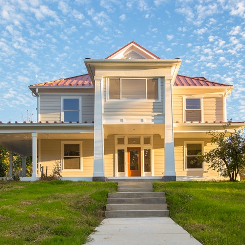 Exterior photo of the front of a 2-story house with yellow siding and a red roof. thumb